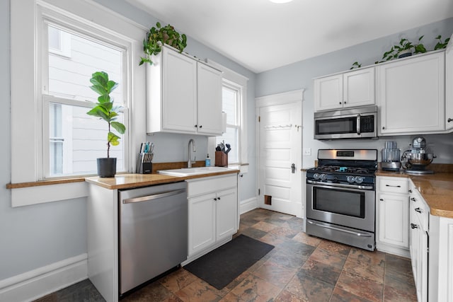 kitchen featuring a sink, white cabinets, stone finish flooring, and stainless steel appliances