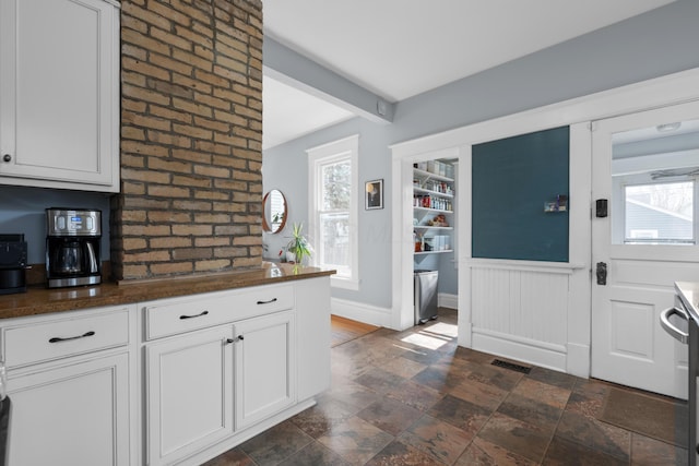 foyer with beam ceiling, visible vents, a healthy amount of sunlight, and stone finish flooring