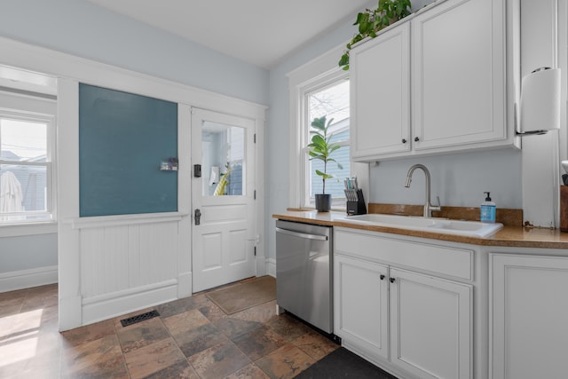 kitchen with visible vents, white cabinets, stainless steel dishwasher, stone finish floor, and a sink