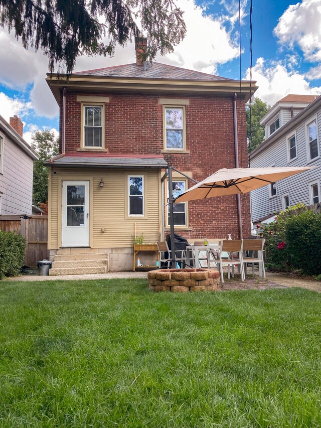 back of house with entry steps, a lawn, brick siding, and a chimney