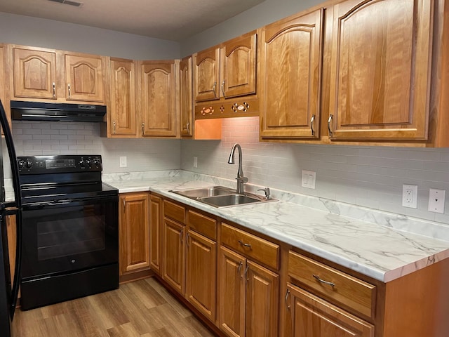 kitchen featuring light wood finished floors, electric range, brown cabinets, under cabinet range hood, and a sink