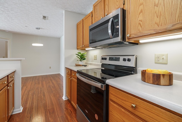 kitchen with dark wood finished floors, light countertops, hanging light fixtures, visible vents, and appliances with stainless steel finishes