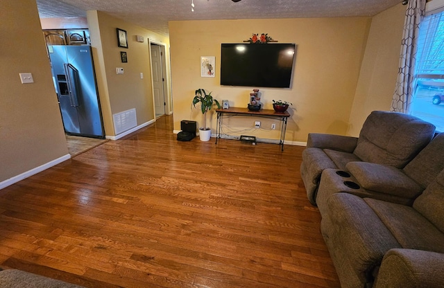 living area with visible vents, a textured ceiling, baseboards, and wood finished floors