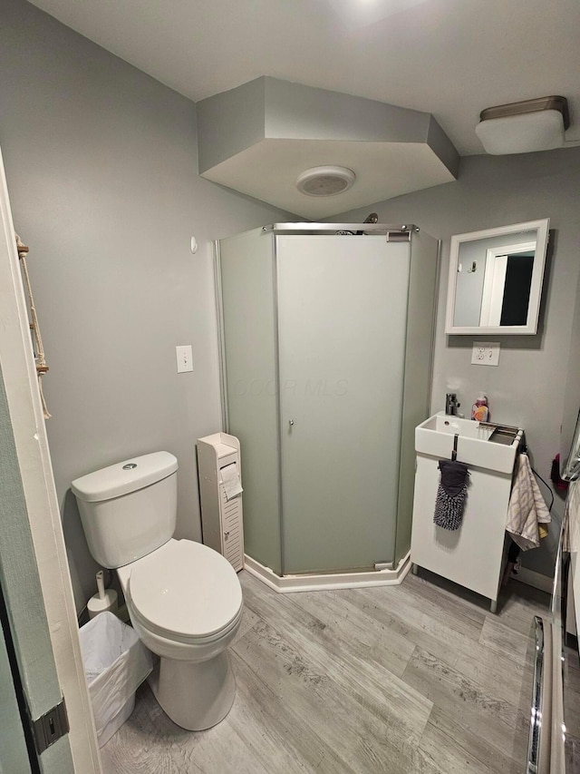 bathroom featuring wood finished floors, toilet, a stall shower, and vanity