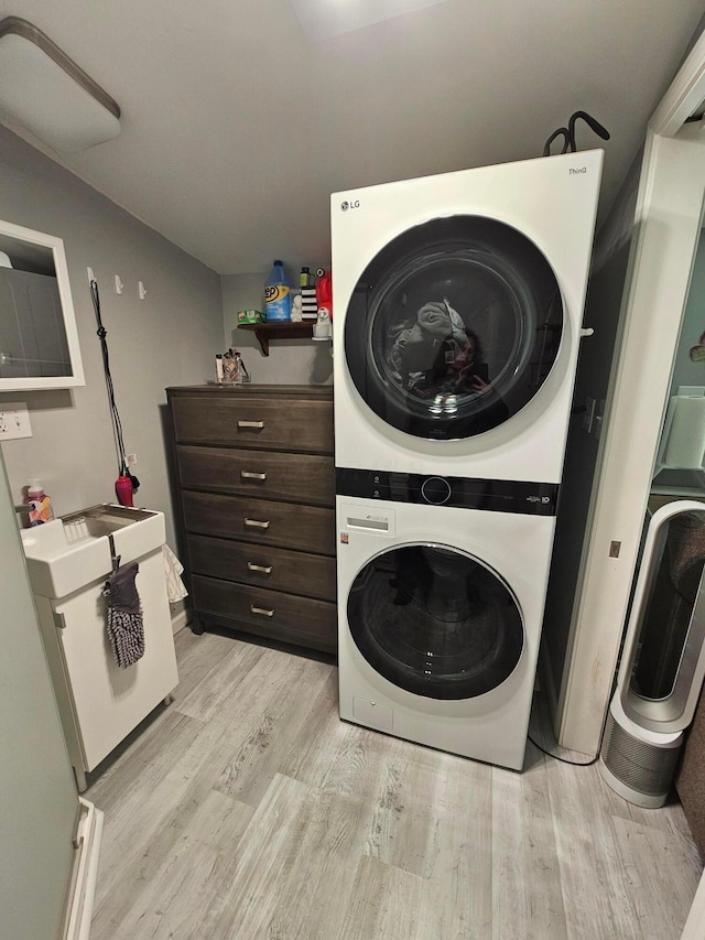 laundry area with light wood-type flooring, stacked washer / drying machine, and laundry area