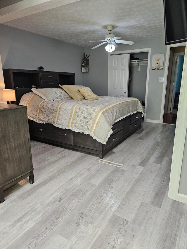 bedroom with a textured ceiling, a closet, light wood-style floors, baseboards, and ceiling fan