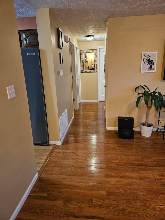 hallway with visible vents, baseboards, a textured ceiling, and wood finished floors