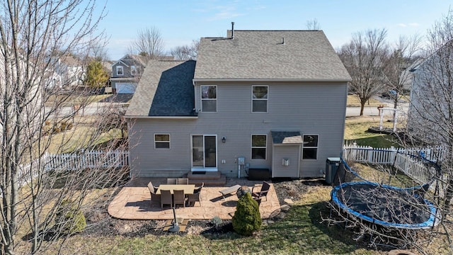 back of house with entry steps, a patio, a fenced backyard, roof with shingles, and a trampoline