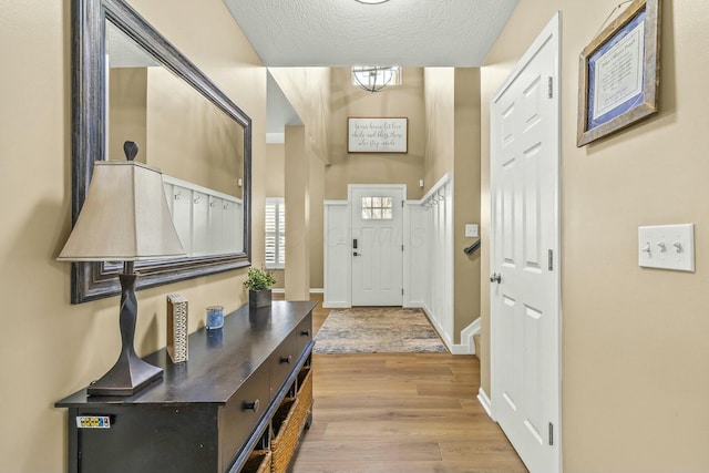 doorway with light wood-style floors, a textured ceiling, and baseboards