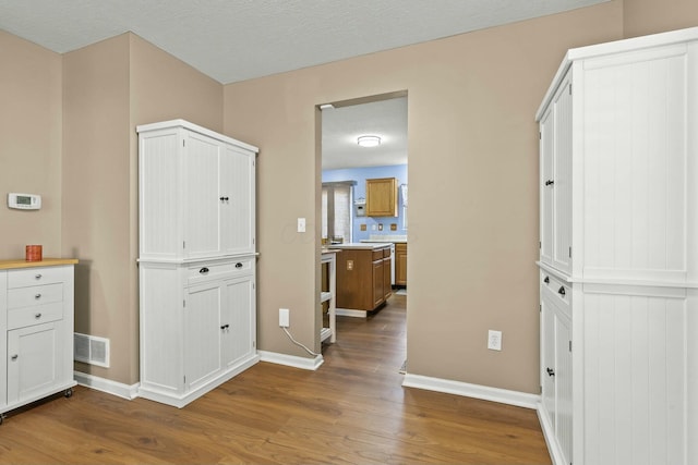 corridor featuring visible vents, a textured ceiling, baseboards, and wood finished floors