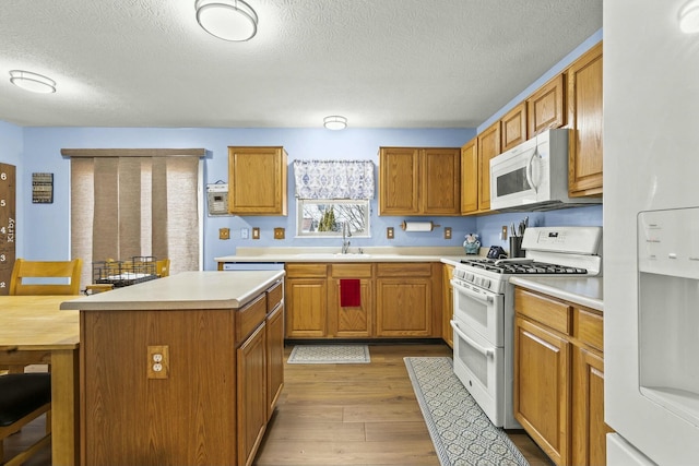 kitchen featuring light wood-type flooring, white appliances, light countertops, and a sink