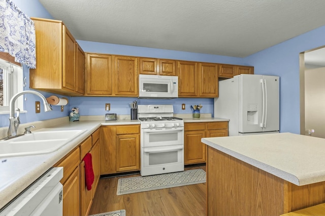 kitchen with light wood finished floors, light countertops, a sink, a textured ceiling, and white appliances