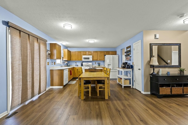 kitchen featuring white appliances, dark wood-style flooring, a sink, visible vents, and light countertops