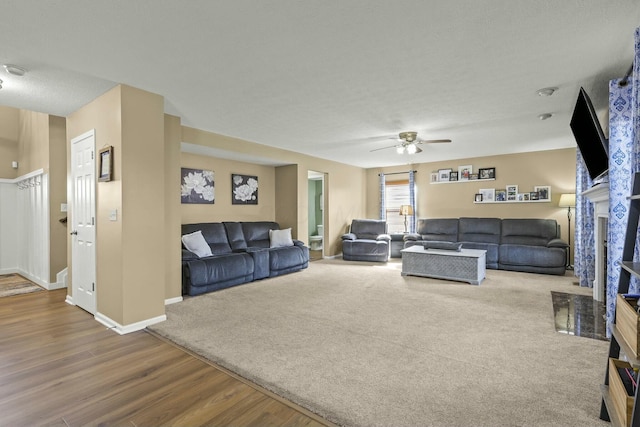 carpeted living room with ceiling fan, a textured ceiling, baseboards, and wood finished floors