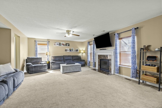 carpeted living room featuring baseboards, a fireplace, a ceiling fan, and a textured ceiling