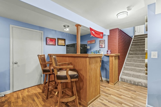 bar featuring light wood finished floors, a dry bar, stairway, and freestanding refrigerator