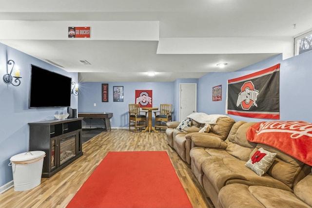 living room featuring a glass covered fireplace, visible vents, baseboards, and wood finished floors