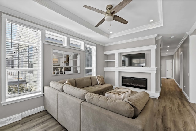 living room featuring baseboards, visible vents, a glass covered fireplace, wood finished floors, and a tray ceiling