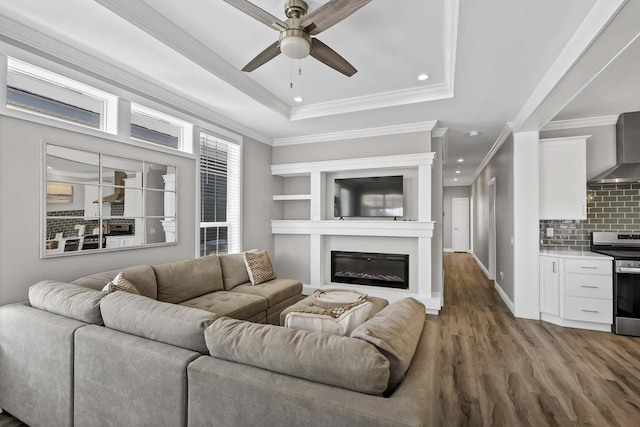 living room featuring a tray ceiling, recessed lighting, a ceiling fan, a glass covered fireplace, and wood finished floors