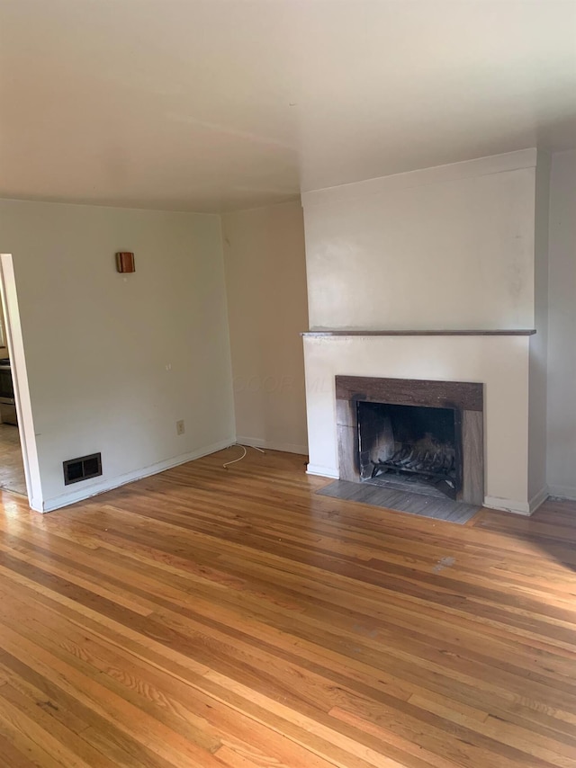 unfurnished living room featuring a fireplace with flush hearth, visible vents, baseboards, and wood finished floors