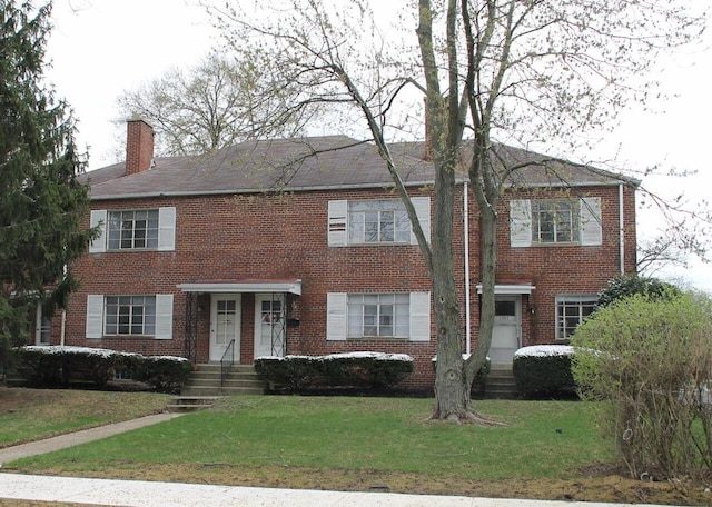 view of front of home with brick siding, a chimney, and a front lawn