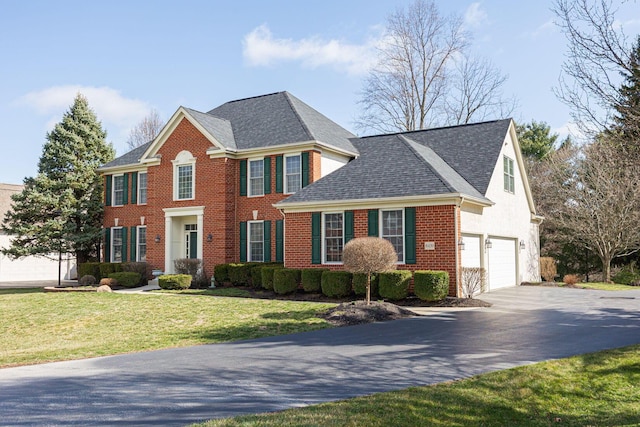 colonial home featuring brick siding, driveway, an attached garage, and a front lawn
