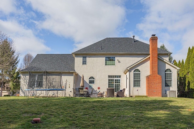 rear view of house with a yard, a trampoline, a chimney, and stucco siding