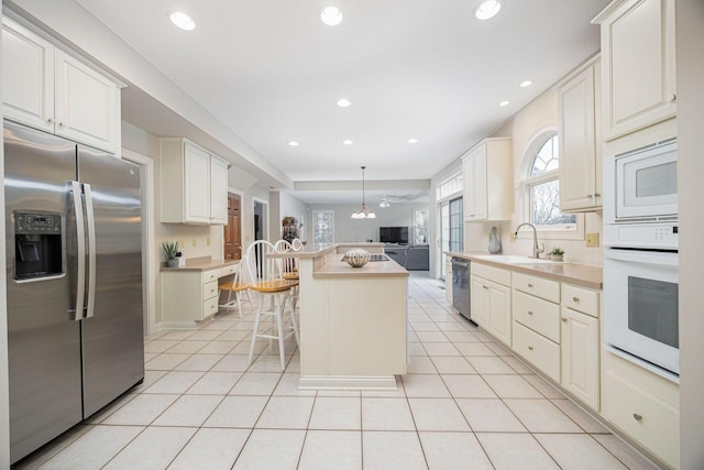 kitchen featuring white appliances, light tile patterned floors, a sink, a kitchen breakfast bar, and a center island