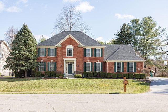 colonial-style house featuring brick siding, a shingled roof, and a front yard