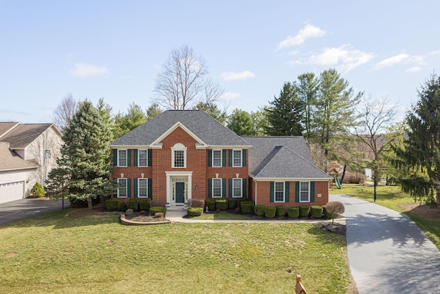 view of front of house with aphalt driveway, a front lawn, brick siding, and a shingled roof
