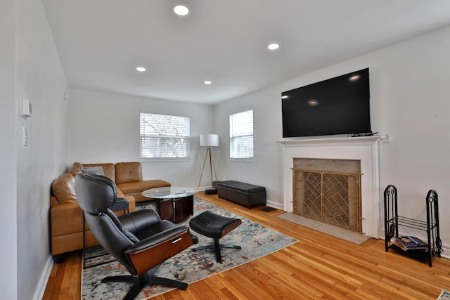 living area with light wood-type flooring, a fireplace with flush hearth, baseboards, and recessed lighting