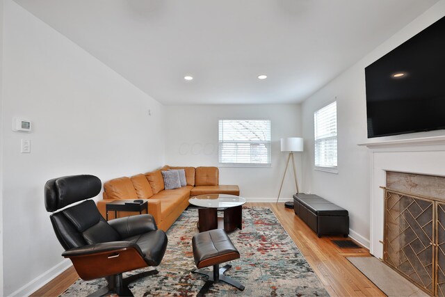 living area featuring light wood-style floors, a fireplace with flush hearth, and baseboards