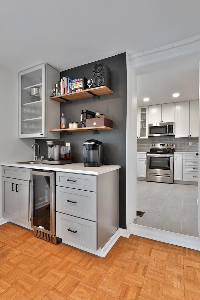 bar with beverage cooler, stainless steel appliances, a sink, decorative backsplash, and wet bar