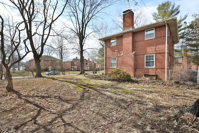 view of side of home with a chimney, fence, and brick siding