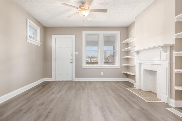 unfurnished living room featuring baseboards, light wood finished floors, a fireplace, ceiling fan, and a textured ceiling