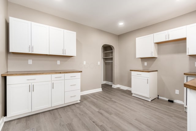 kitchen with white cabinetry, baseboards, arched walkways, and light wood-type flooring