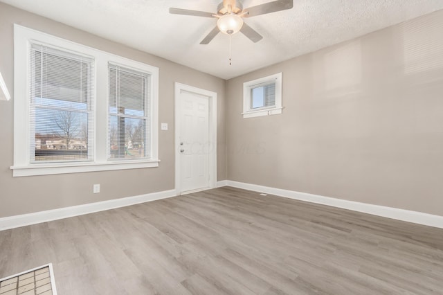 empty room with baseboards, a textured ceiling, wood finished floors, and a ceiling fan