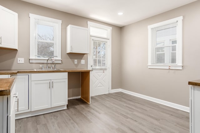 kitchen with baseboards, wooden counters, light wood-style flooring, a sink, and white cabinetry