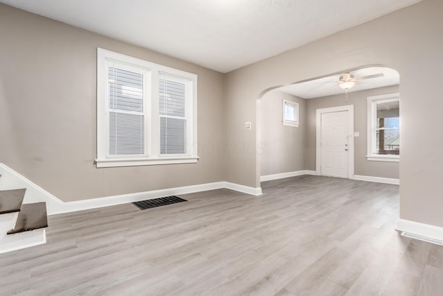 empty room with visible vents, baseboards, wood finished floors, arched walkways, and a ceiling fan