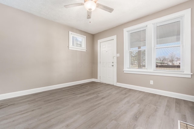 unfurnished room featuring light wood-type flooring, baseboards, a textured ceiling, and a ceiling fan