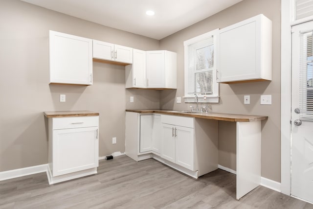 kitchen with white cabinets, baseboards, light wood-type flooring, and a sink