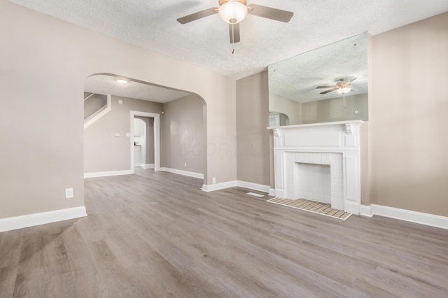 unfurnished living room featuring wood finished floors, baseboards, a fireplace, arched walkways, and a textured ceiling