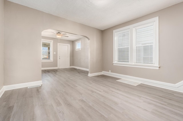 empty room with ceiling fan, baseboards, wood finished floors, arched walkways, and a textured ceiling