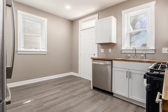 kitchen with baseboards, a sink, stainless steel appliances, light wood-style floors, and white cabinetry