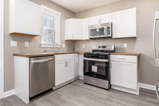 kitchen with white cabinets, stainless steel appliances, light wood-style flooring, and a sink