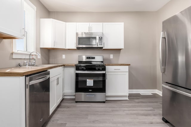 kitchen with baseboards, light wood finished floors, a sink, appliances with stainless steel finishes, and white cabinetry