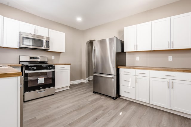 kitchen featuring white cabinetry, arched walkways, light wood-style floors, appliances with stainless steel finishes, and wooden counters