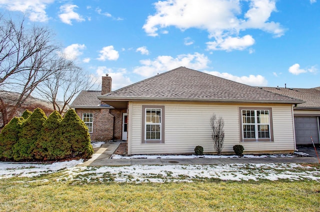 snow covered house with a chimney, a lawn, and roof with shingles