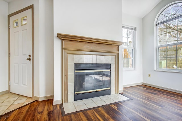 room details featuring a tiled fireplace, wood finished floors, and baseboards