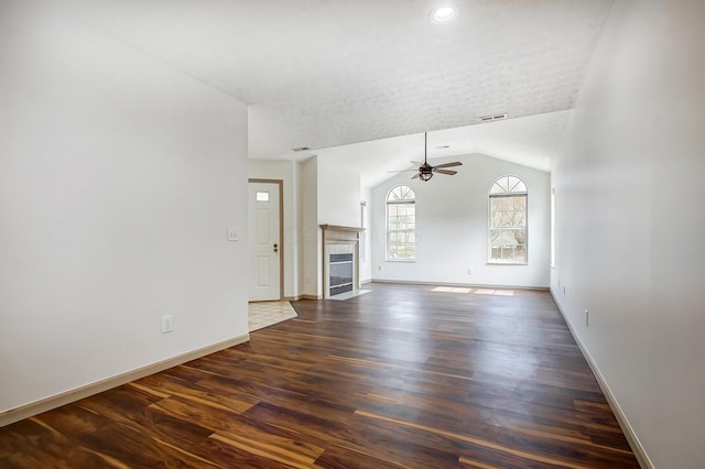 unfurnished living room with visible vents, a ceiling fan, a tile fireplace, dark wood-style floors, and vaulted ceiling